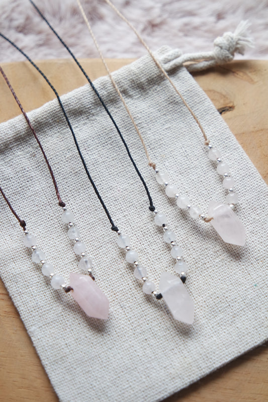 „Handgemachte Rosenquarz-Kette auf braunem Band mit Silber- und Messingdetails auf Leinenbeutel.“