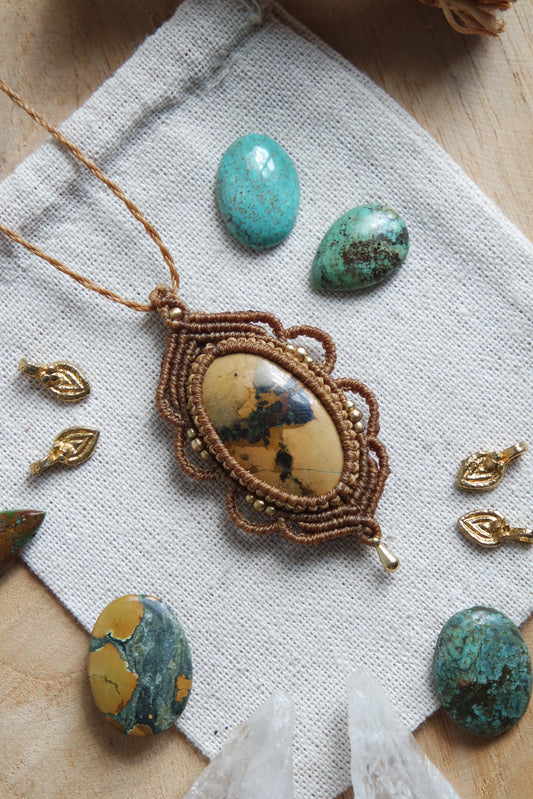 Makramee-Kette ‚Wächterindestürkis‘ mit grünlich gemasertem Türkisstein – liegend auf hellem Leinenbeutel mit dekorativen Edelsteinen