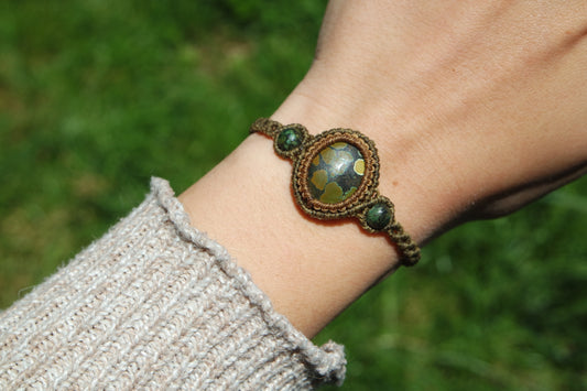 Makramee-Armband ‚Lichtbrunnen‘ mit goldgrünem Naturstein – getragen am Handgelenk mit beigem Strickpulli, bei Sonnenlicht fotografiert