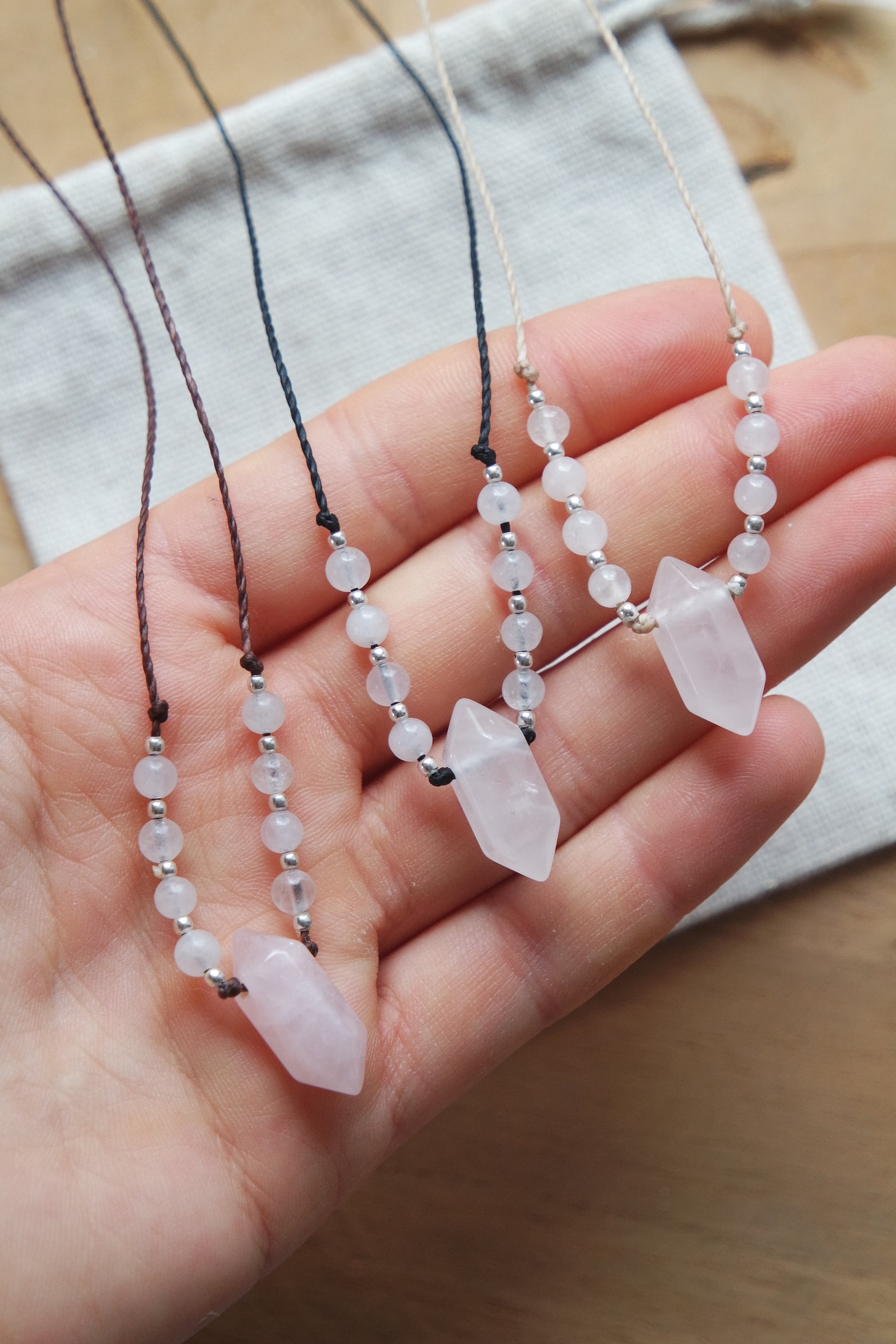 „Zarte Rosenquarz-Kette auf beigem Faden, handgeknüpft mit kleinen hell rosa Perlen und silberdetails.“