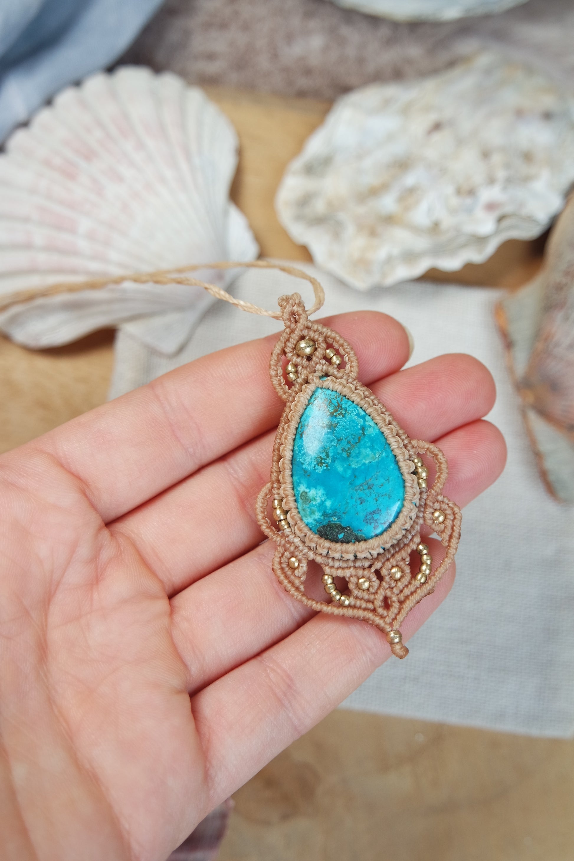 Handgeknüpfte Makramee Kette Strandseele mit blauem Chrysokoll und Messingperlen in sandfarbenem Makramee auf einer Hand liegend.