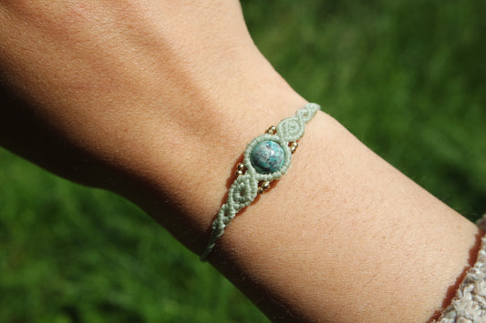 „Makramee-Armband ‚Aquablau‘ mit runder Türkisperle und goldenen Messingperlen – getragen am Handgelenk bei Sonnenlicht“