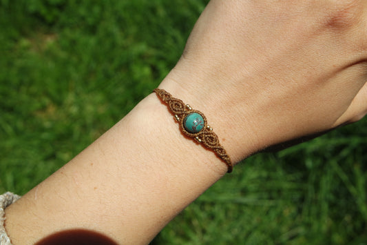 Makramee-Armband ‚Sonnenfunkeln‘ mit Türkisperle und goldenen Messingperlen – getragen am Handgelenk im Sonnenlicht auf grünem Hintergrund