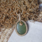 Handgefertigte Makramee Kette Mossalia mit ovaler grüner Jade, heller Einfassung und kleiner goldfarbener Edelstahl-Blüte.