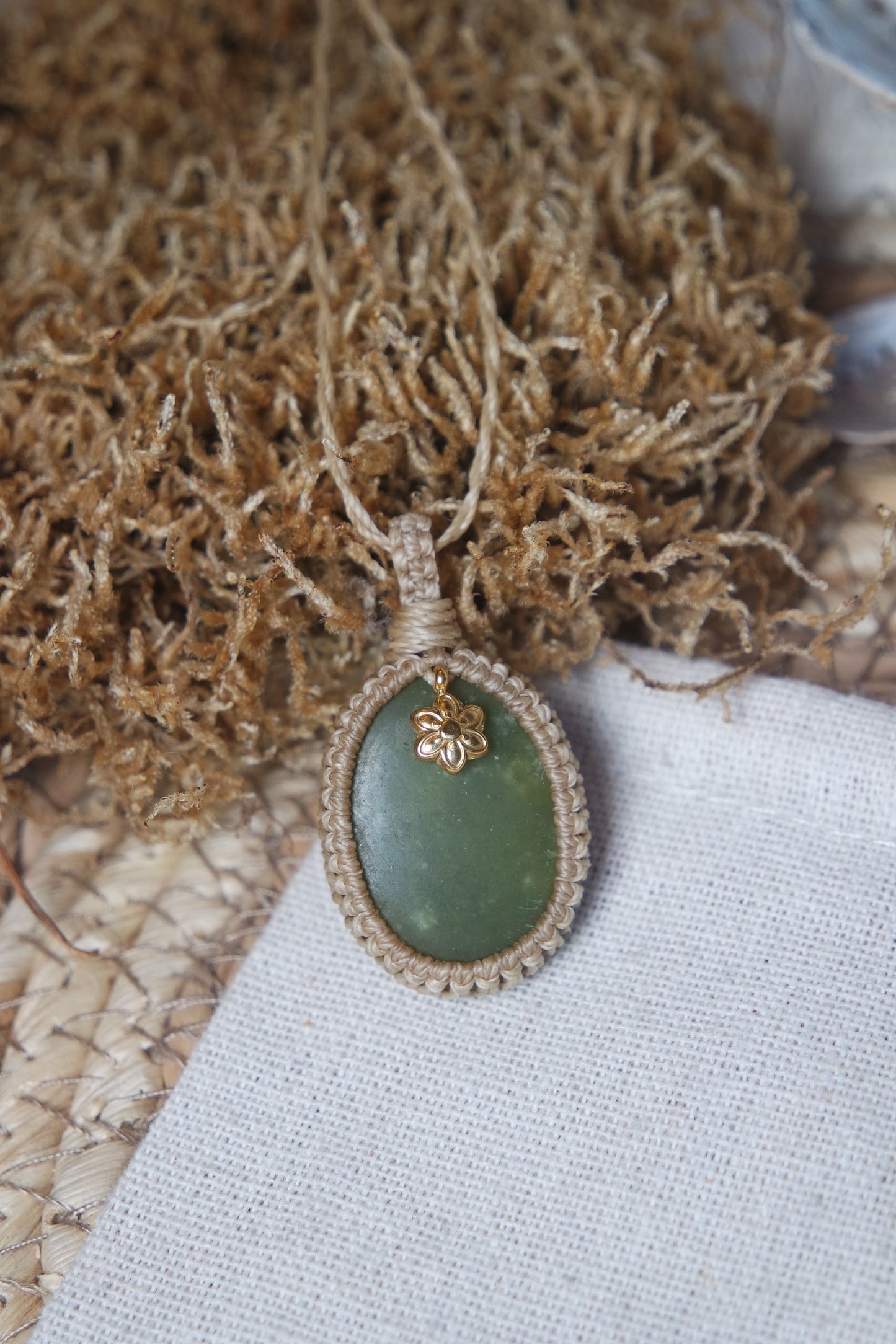 Handgefertigte Makramee Kette Mossalia mit ovaler grüner Jade, heller Einfassung und kleiner goldfarbener Edelstahl-Blüte.